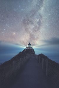 Illuminated lighthouse at coastline against star field during night