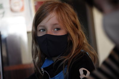 7 year old girl with a blue face mask with dark blond hair is looking towards the camera.