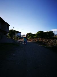 Rear view of man standing by building against clear sky