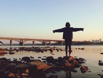 Man standing on rock by bridge against sky