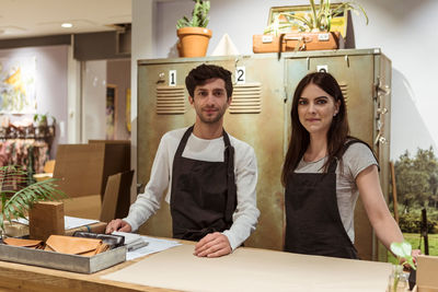 Portrait of confident male and female coworkers standing at checkout counter