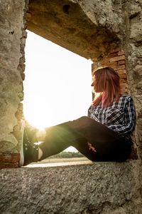 Red-haired girl sitting in a window of a building at sunset