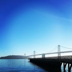 Suspension bridge over sea against clear blue sky