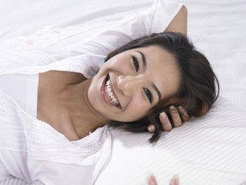 Close-up portrait of smiling woman lying down on bed at home