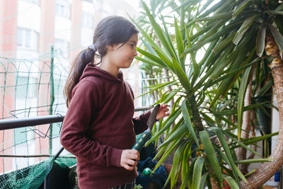 Standing girl with dark hair on the balcony taking care of the home plants