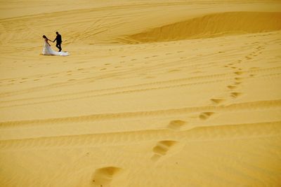 Distant view of bride and groom walking while holding hands at desert