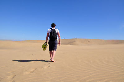 Full length rear view of man walking on desert