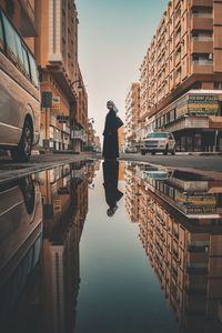 Rear view of man on canal amidst buildings in city