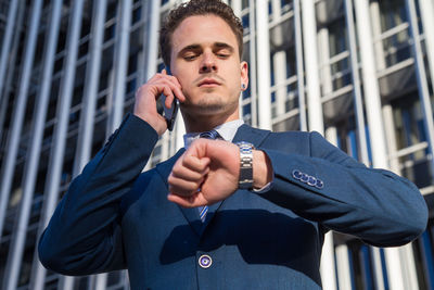 Low angle view of businessman talking on smart phone while standing against building