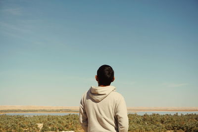 Rear view of man standing against landscape and clear sky