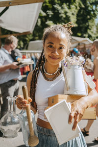 Smiling young woman holding different objects while shopping at flea market