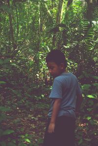 Boy standing by trees in forest