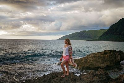 Full length of woman standing on rock at sea shore against sky