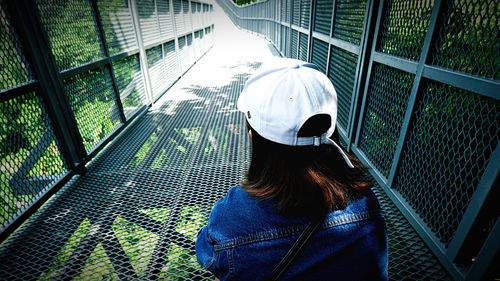 Rear view of woman wearing cap while sitting on footbridge