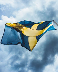 Low angle view of swedish flag against cloudy sky