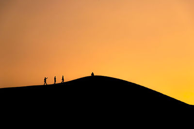Silhouette people against orange sky during sunset