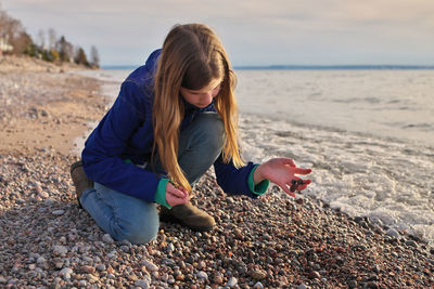 Young adolescent girl collects beautiful colorful rocks, pebbles and shells on the beach