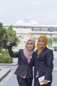 Happy businesswoman showing something to colleague while standing on street