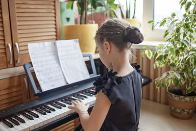 Rear view of girl playing piano at home