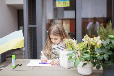 Small girl draws ukrainian flag in safe place abroad in europe where she fled from russian invasion