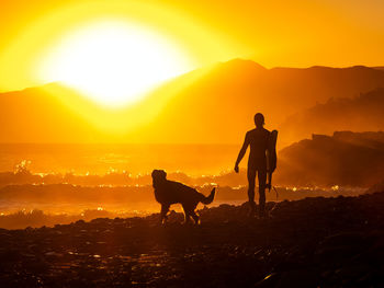 Silhouette man with arms outstretched against orange sky