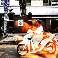 Man riding motor scooter on street against building