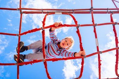 Directly below shot of boy playing on jungle gym against sky