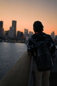 Rear view of man standing by river against sky during sunset