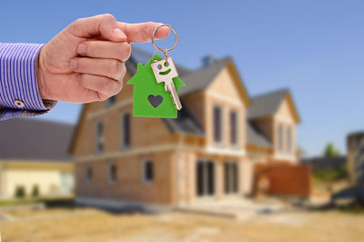 Cropped hand of man holding key ring against house