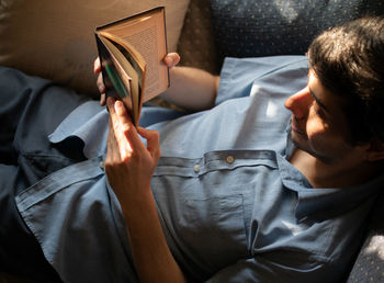 Smiling man reading book while lying on bed at home