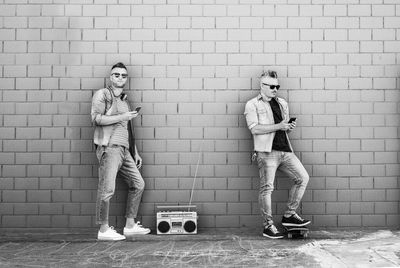 Full length portrait of men standing by radio against wall outdoors