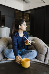 Young businesswoman with coffee cup and fruit bowl sitting in cafeteria at office