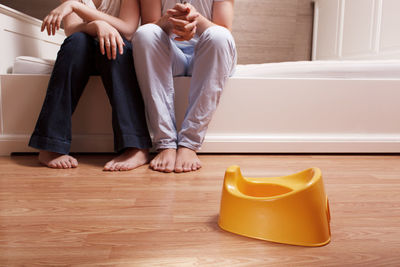 Low section of man and woman sitting on bed in front of yellow toilet bowl