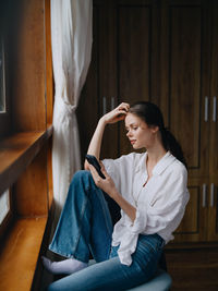 Side view of young woman sitting on bed at home