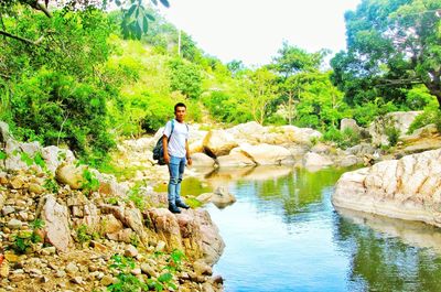 Man standing on rock by trees against sky