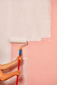 The painter's female hands hold a paint roller on a long telescopic rod .