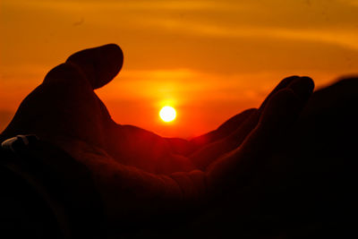 Close-up of silhouette hand against orange sky