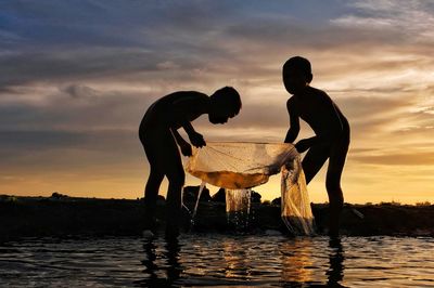 Silhouette people on water against sky during sunset