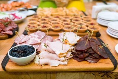Wooden board with slices of meat types jerky, ham, bowl of caramelized onions