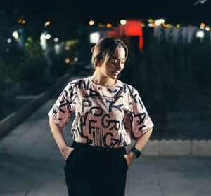 Portrait of young woman standing against illuminated city at night