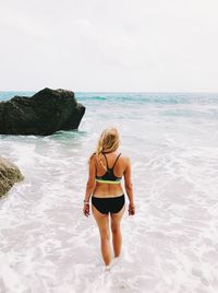 Rear view of woman standing by rock at beach against sky