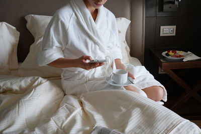 Midsection of woman holding mobile phone while sitting on bed