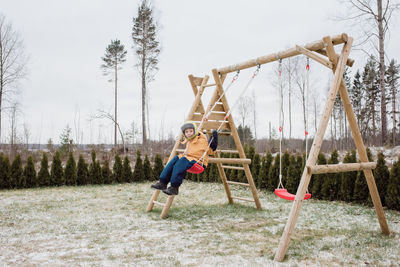 Boy sat on a swing swinging outside in his garden in the snow