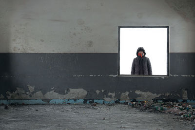 Hooded man seen through window in abandoned building