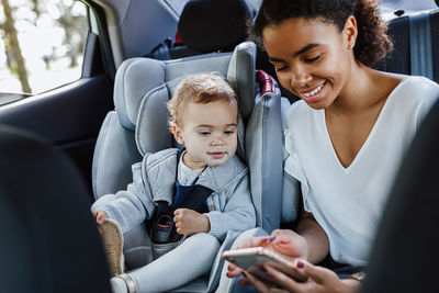 Mother with daughter while hold holding smart phone sitting in car