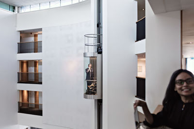 Businesswoman standing in balcony while businessman with son in elevator at office