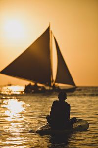 Silhouette boy paddleboarding in sea against sky during sunset