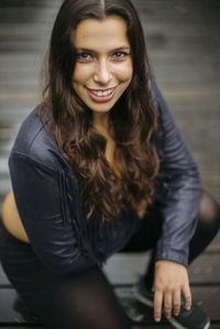 Portrait of smiling young woman crouching on wood