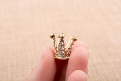Close-up of hand holding crown shape jewelry on table