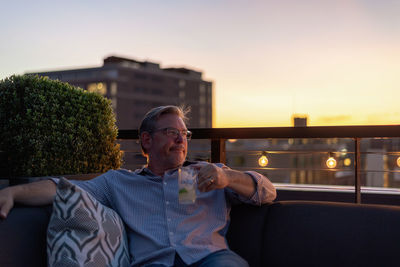 Man looking away while sitting against sky during sunset